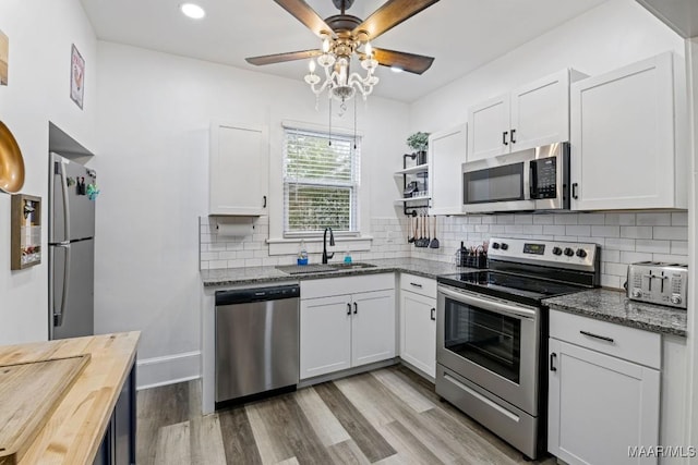 kitchen with stainless steel appliances, a sink, white cabinetry, open shelves, and dark stone countertops