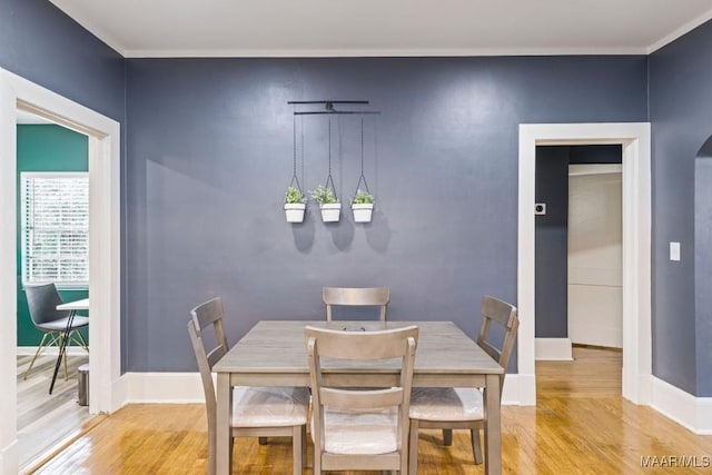 dining space featuring arched walkways, light wood-style flooring, and baseboards