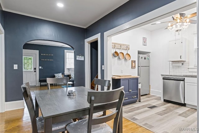 dining space featuring light wood-style floors, arched walkways, ornamental molding, and baseboards