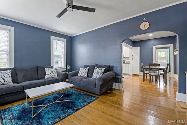 living room featuring baseboards, arched walkways, ceiling fan, ornamental molding, and wood finished floors