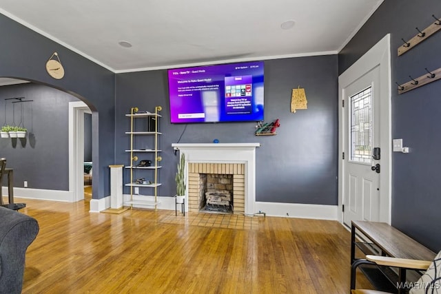 living area featuring arched walkways, a fireplace, wood finished floors, baseboards, and ornamental molding