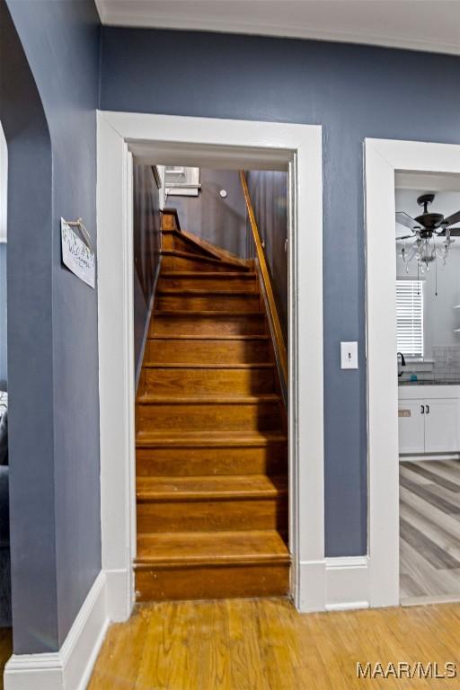 staircase with arched walkways, ornamental molding, ceiling fan, wood finished floors, and baseboards