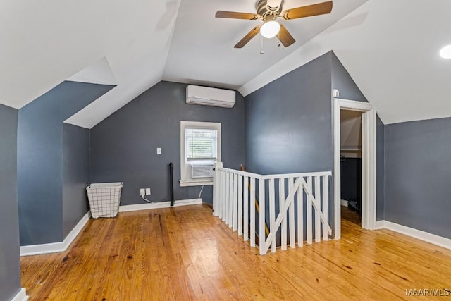 additional living space with baseboards, vaulted ceiling, wood finished floors, and a wall mounted air conditioner