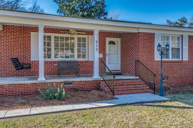 view of exterior entry with crawl space, covered porch, and brick siding