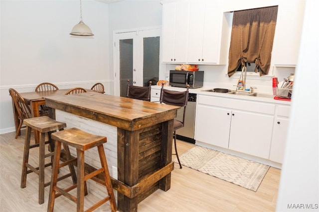 kitchen with white cabinets, light wood-style flooring, hanging light fixtures, stainless steel appliances, and light countertops