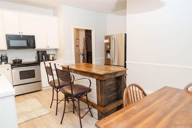 kitchen with light wood finished floors, white cabinetry, stainless steel appliances, and light countertops