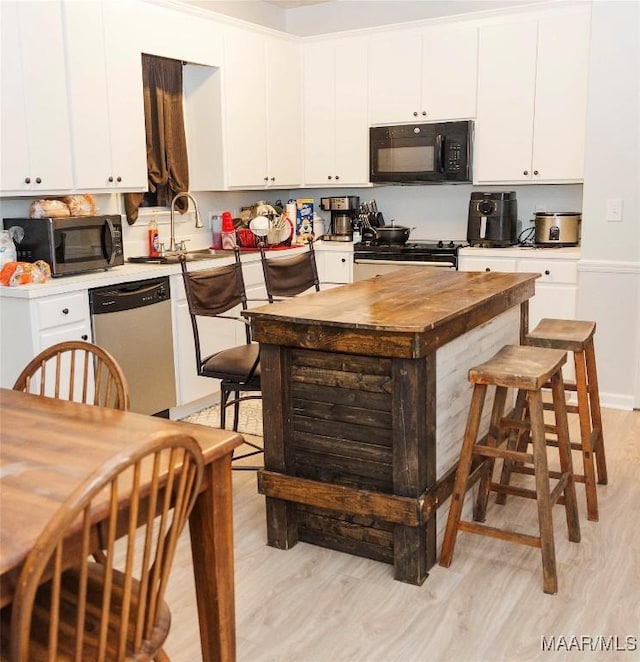 kitchen with stainless steel appliances, a sink, white cabinets, light wood-type flooring, and a center island