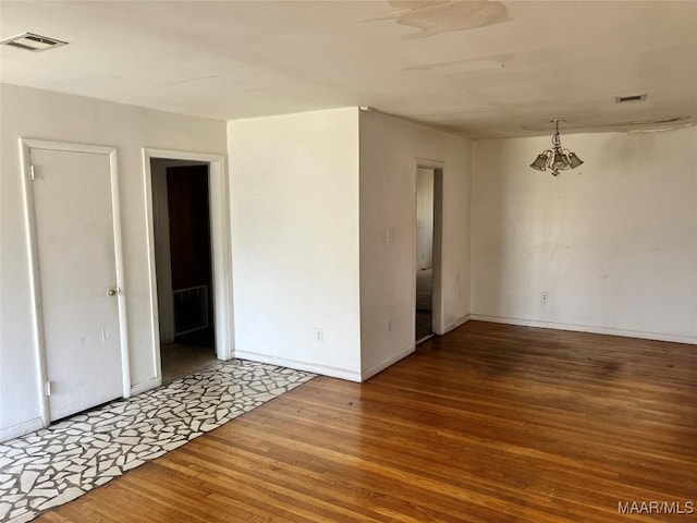 spare room featuring baseboards, wood finished floors, visible vents, and a notable chandelier