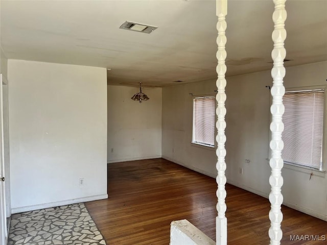 empty room featuring dark wood-style flooring, visible vents, and baseboards