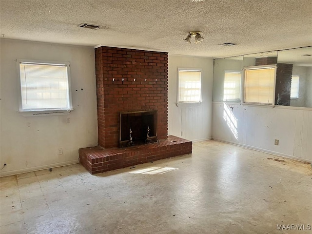 unfurnished living room featuring a brick fireplace, visible vents, concrete floors, and a textured ceiling