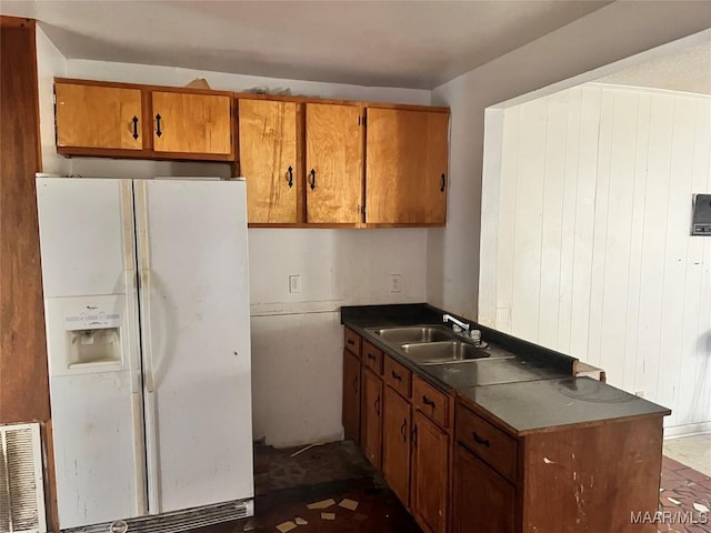 kitchen with white refrigerator with ice dispenser, visible vents, dark countertops, brown cabinets, and a sink