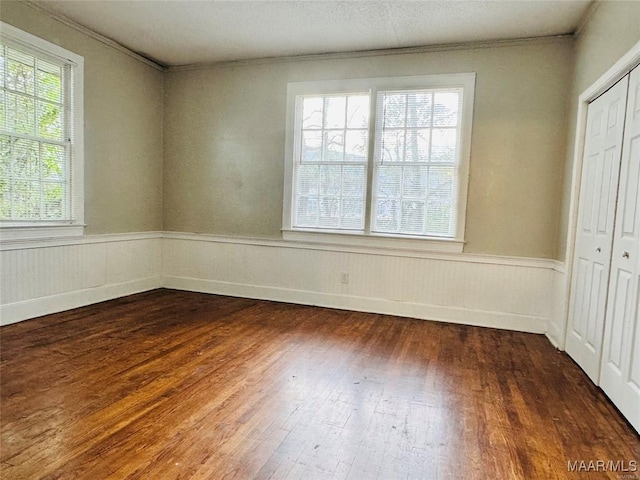 empty room featuring dark wood finished floors, crown molding, and wainscoting