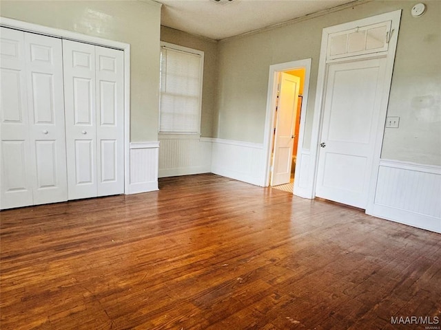 unfurnished bedroom with a closet, wood finished floors, and wainscoting