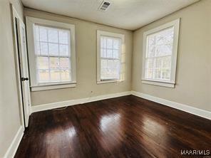 unfurnished room featuring visible vents, baseboards, and dark wood-style flooring