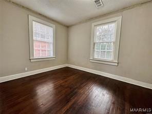 empty room with wood finished floors, visible vents, and baseboards