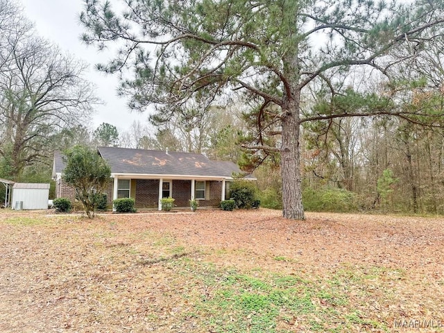 ranch-style home with an outbuilding, covered porch, brick siding, and a shed