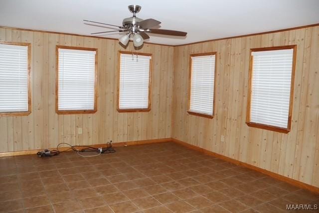 empty room with a ceiling fan, baseboards, crown molding, and wood walls