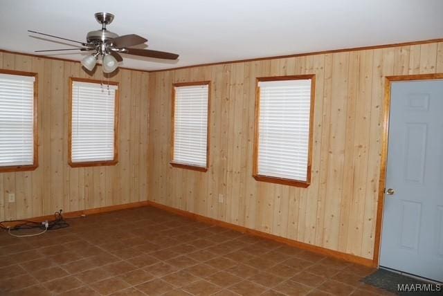 empty room featuring ornamental molding, wood walls, baseboards, and a ceiling fan