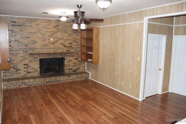 unfurnished living room featuring dark wood-style floors, ceiling fan, a fireplace, and crown molding