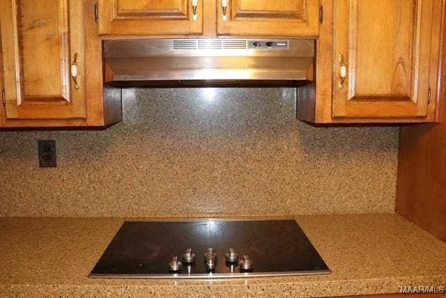 kitchen featuring light countertops, brown cabinets, black electric cooktop, and under cabinet range hood