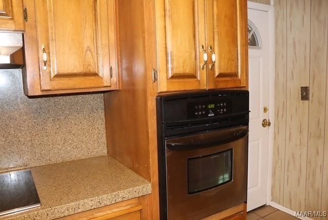 kitchen with wall oven, light tile patterned floors, black electric stovetop, and brown cabinetry