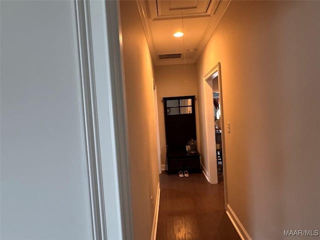 hall featuring dark wood-type flooring, visible vents, baseboards, ornamental molding, and attic access