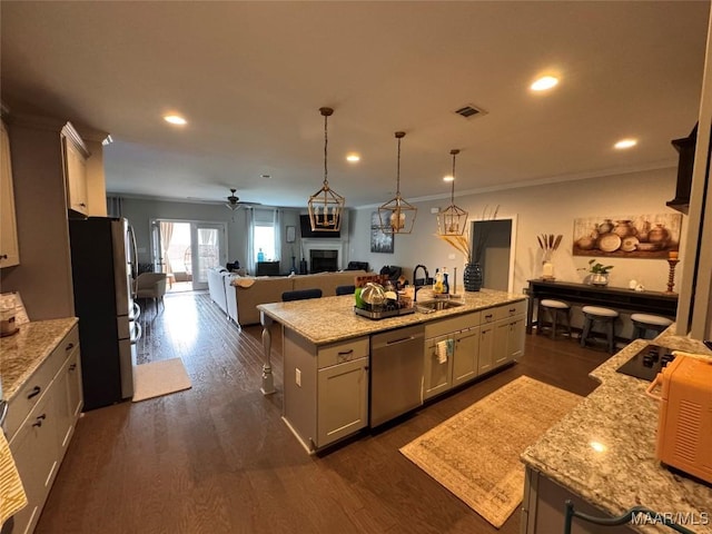 kitchen with an island with sink, appliances with stainless steel finishes, open floor plan, a fireplace, and a sink