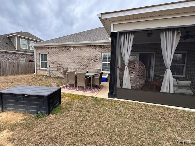 back of property with roof with shingles, brick siding, a lawn, a ceiling fan, and fence