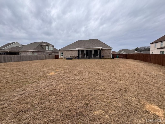 back of house with a fenced backyard, a shingled roof, and brick siding