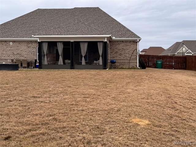 back of house featuring brick siding, a shingled roof, fence, a sunroom, and a lawn