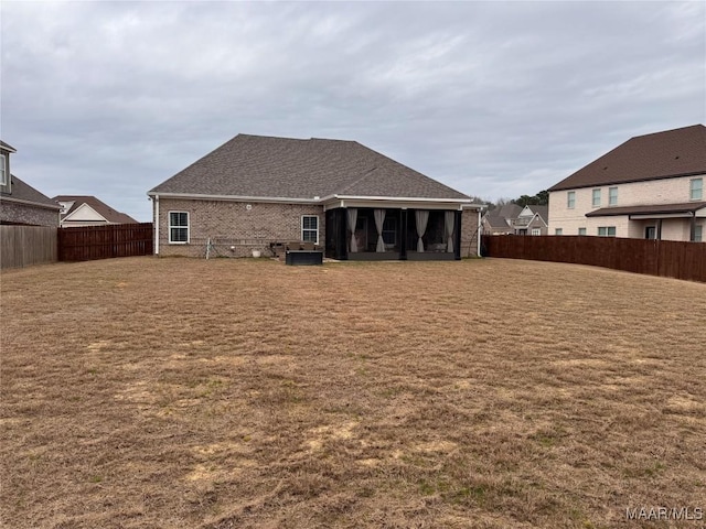 rear view of house featuring a fenced backyard, a lawn, a shingled roof, and brick siding