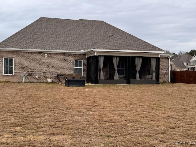 back of house with a shingled roof, a sunroom, fence, a yard, and brick siding