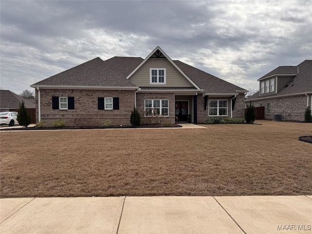 craftsman-style house with a shingled roof, a front yard, and brick siding