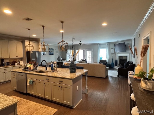 kitchen featuring appliances with stainless steel finishes, light stone counters, open floor plan, a kitchen island with sink, and pendant lighting