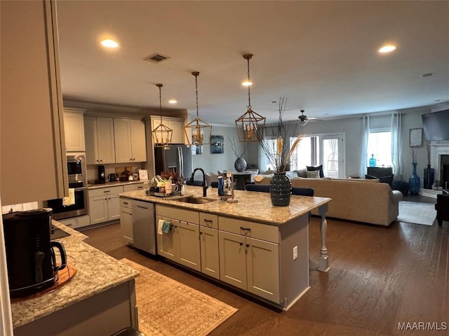 kitchen with a center island with sink, appliances with stainless steel finishes, open floor plan, hanging light fixtures, and a sink