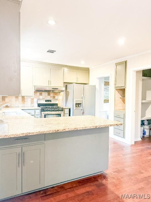 kitchen with stainless steel gas range oven, under cabinet range hood, a sink, light stone countertops, and white fridge with ice dispenser