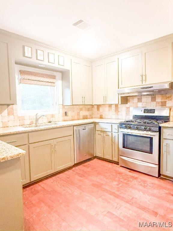 kitchen with appliances with stainless steel finishes, backsplash, a sink, and under cabinet range hood