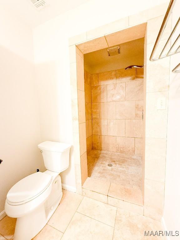 full bathroom with toilet, baseboards, tiled shower, and tile patterned floors