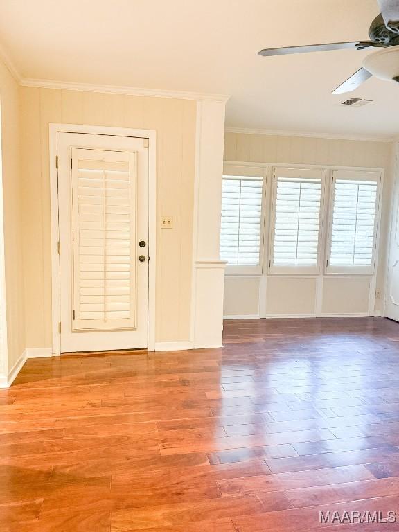 unfurnished room with visible vents, ornamental molding, a ceiling fan, a healthy amount of sunlight, and wood finished floors