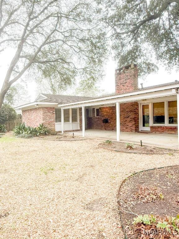 back of house featuring a patio area, brick siding, driveway, and a chimney