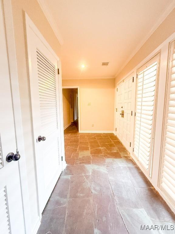 interior space with ornamental molding, stone finish floor, visible vents, and baseboards