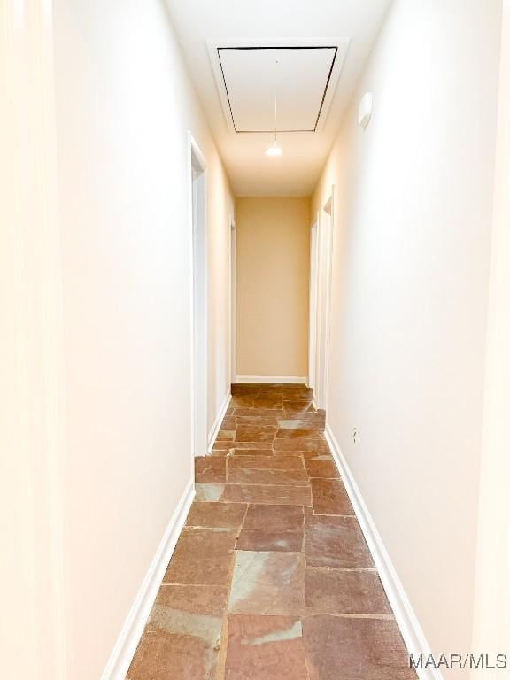 hall with attic access, stone finish floor, and baseboards