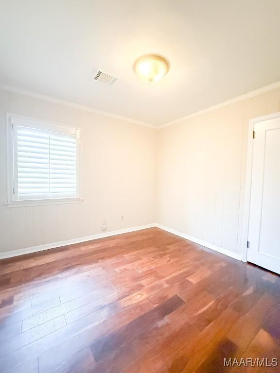 empty room featuring ornamental molding, visible vents, baseboards, and wood finished floors