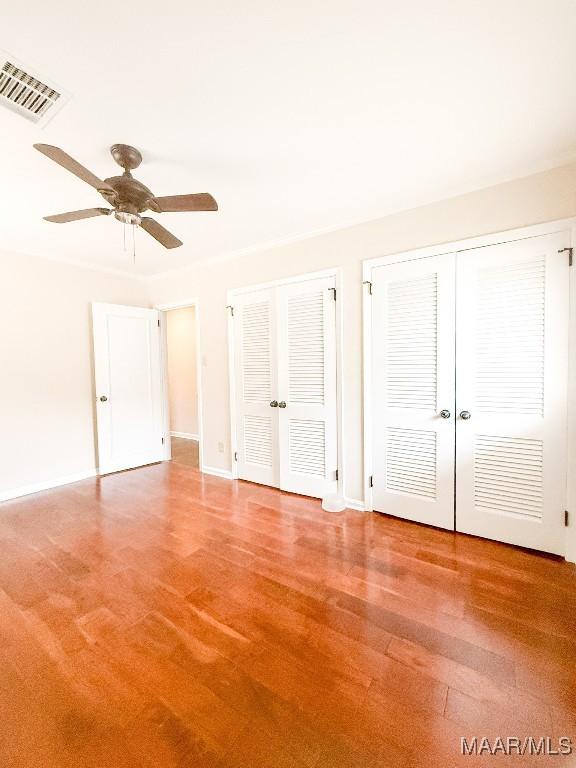 unfurnished bedroom with two closets, visible vents, a ceiling fan, wood finished floors, and baseboards