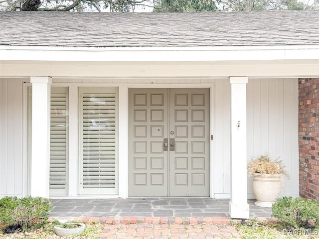 entrance to property with a shingled roof, a porch, and brick siding