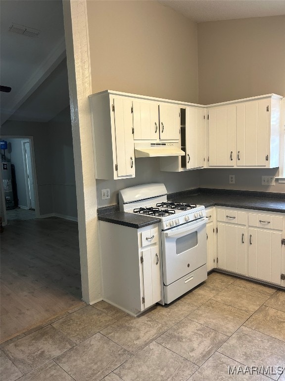 kitchen featuring dark countertops, under cabinet range hood, white gas range, and white cabinets