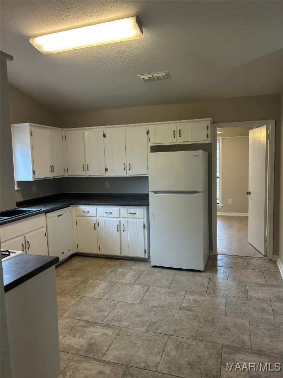 kitchen with white appliances, visible vents, dark countertops, a textured ceiling, and white cabinetry