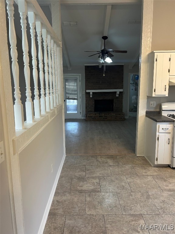 interior space with white cabinetry, a ceiling fan, a brick fireplace, range, and dark countertops