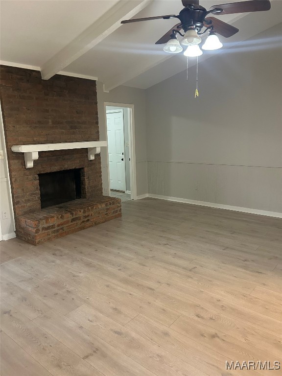 unfurnished living room featuring a wainscoted wall, a fireplace, lofted ceiling with beams, a ceiling fan, and light wood-type flooring