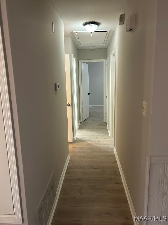 hall with attic access, visible vents, baseboards, and wood finished floors